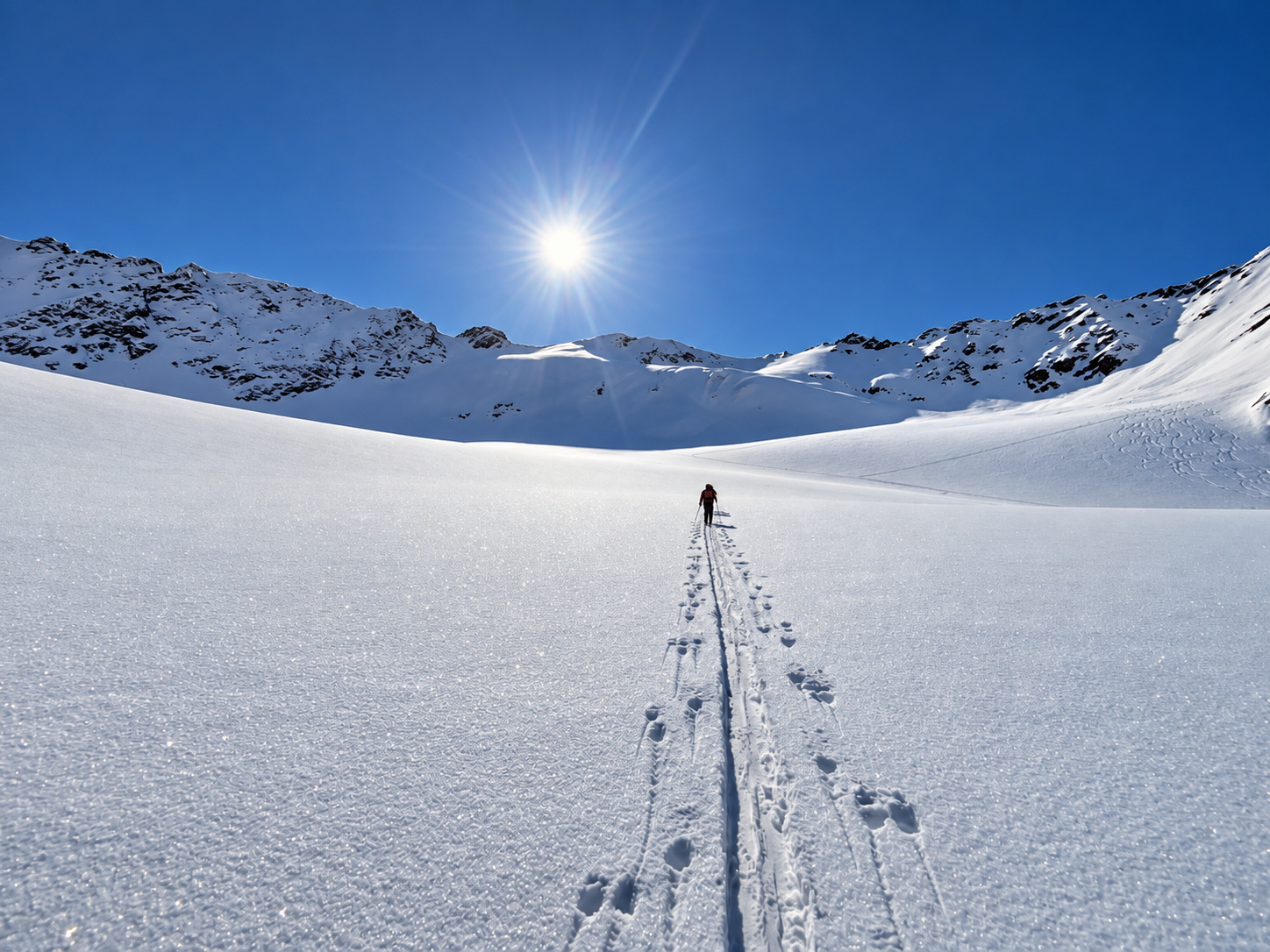 Ski tourer following an ascent track through a wide snow-covered mountain basin